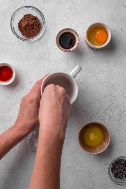 Butter in ceramic mug being stirred with hands.