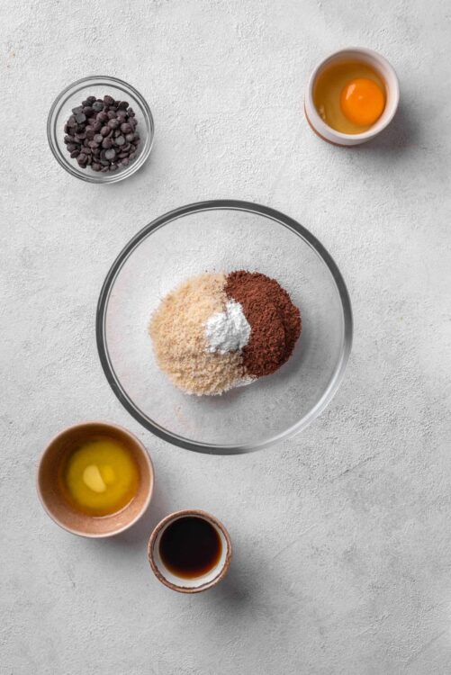 Chocolate chips, dry ingredients, eggs, vanilla extract, and soy sauce in bowls for baking.