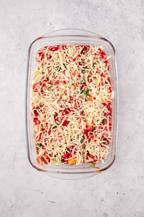 Baked Ziti with shredded cheese and vegetables in a glass baking dish.