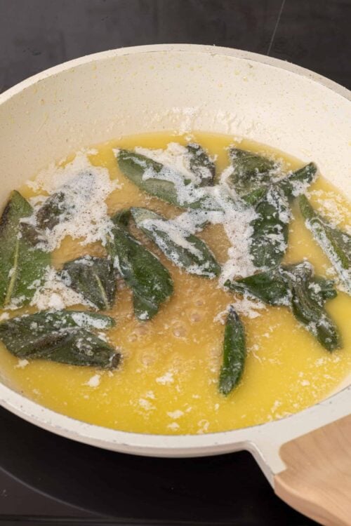 Savory sage butter sauce cooking in a skillet with fresh sage leaves.