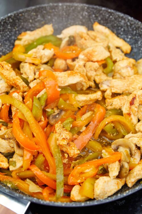 Sautéed chicken and colorful bell peppers in a black skillet.