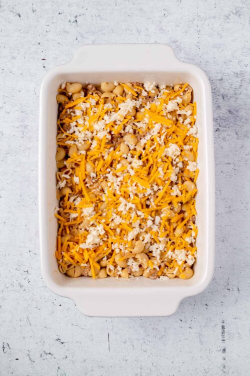 Creamy baked macaroni and cheese in a white casserole dish with shredded cheddar cheese and white cheese topping.