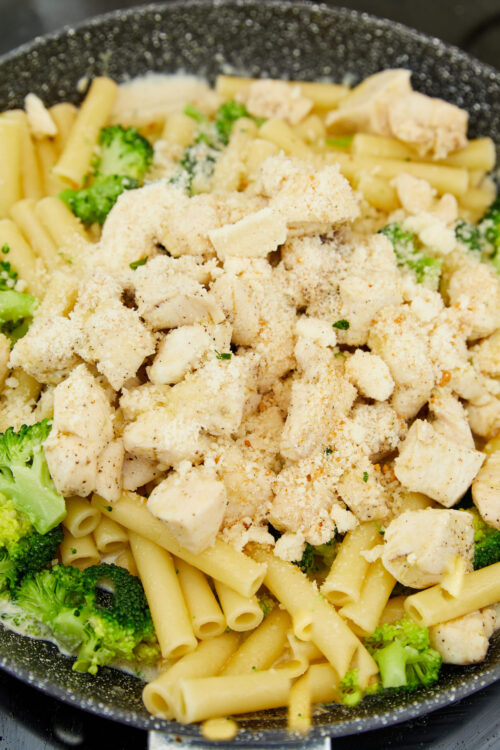 Creamy chicken pasta with broccoli in a skillet, topped with grated cheese and bread crumbs.