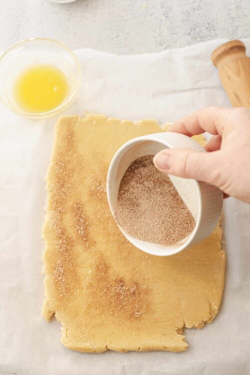 Butter cookie dough being seasoned with cinnamon, with a bowl of melted butter in the background.
