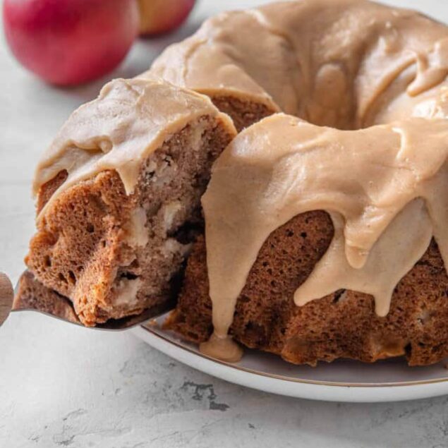 Apple cinnamon coffee cake with glaze on a white plate with apples in the background.
