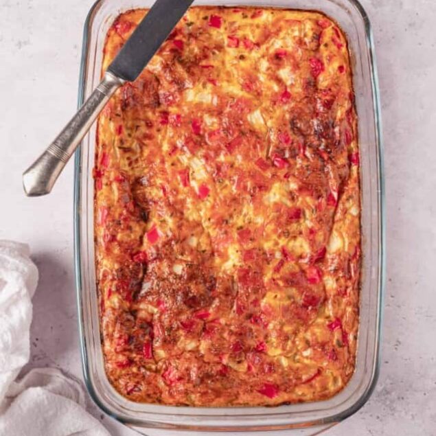 Baked cheesy baked casserole with red peppers in glass baking dish.