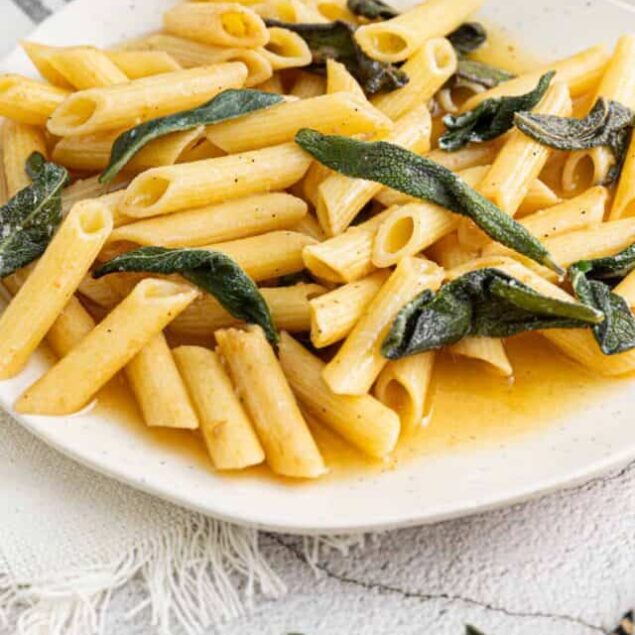 Pasta with sage and butter sauce on a white plate, side of Parmesan cheese, rustic table setting.