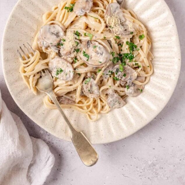 Creamy mushroom pasta dish served on a beige plate with fresh herbs and grated cheese.