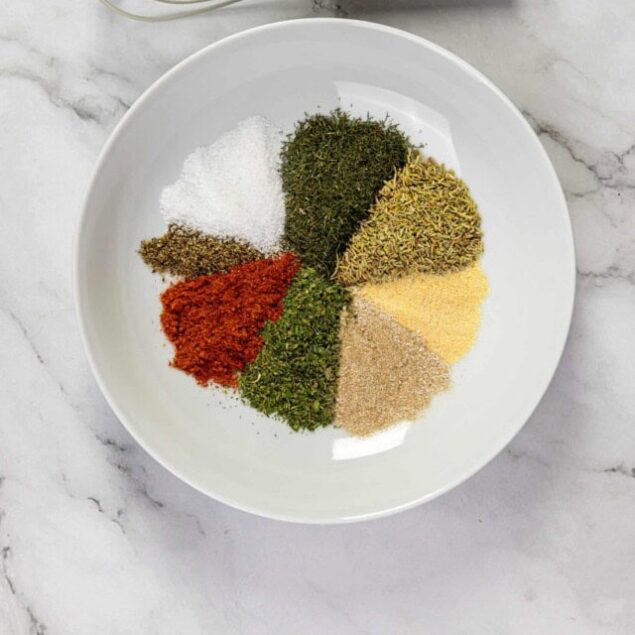 Dried herbs and spices in a white bowl, top view.