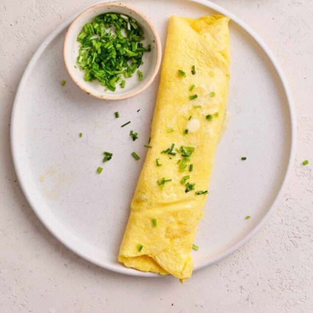 Fluffy scrambled eggs with chopped green onions on a white plate, garnished with fresh herbs.