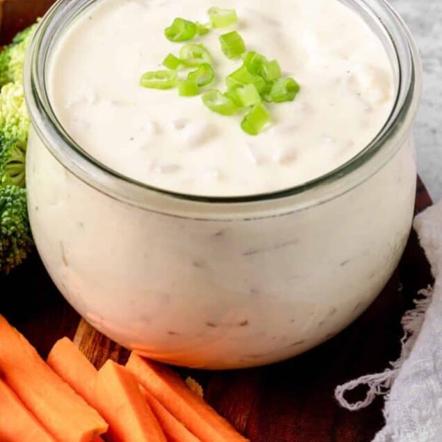 Creamy ranch dip with chopped green onions in a glass jar, served with fresh vegetables for snacking or appetizers.