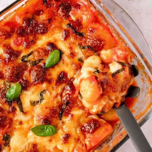 Creamy baked ziti with melted cheese and fresh basil in a glass baking dish.