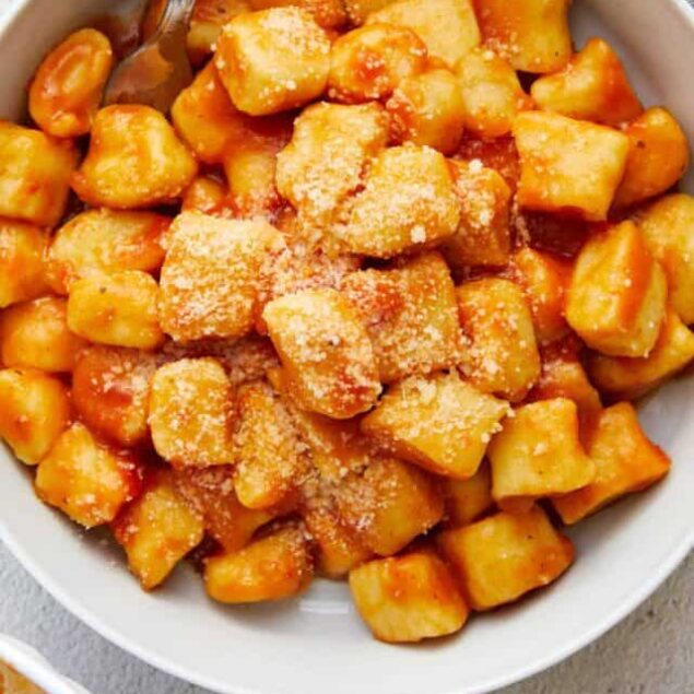 Crispy cheese tortellini with tomato sauce and grated Parmesan cheese in a white bowl.