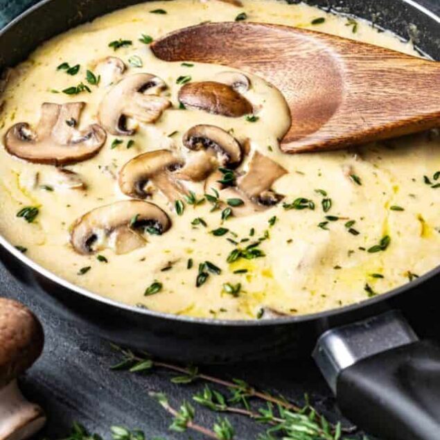 Creamy mushroom and thyme sauce cooking in a skillet with fresh herbs and mushrooms.