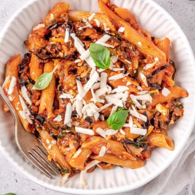 Creamy tomato pasta with basil, cheese, and sautéed vegetables on a white plate.