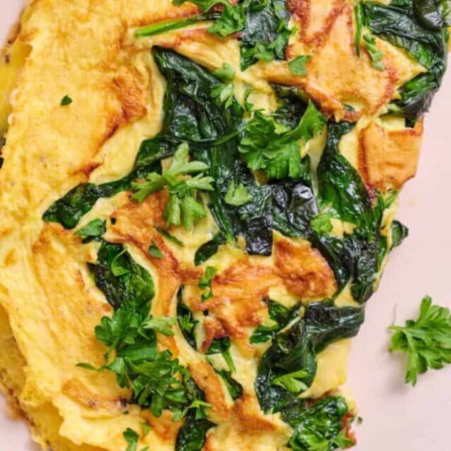 Creamy spinach and cheese omelette with fresh herbs on a white plate.