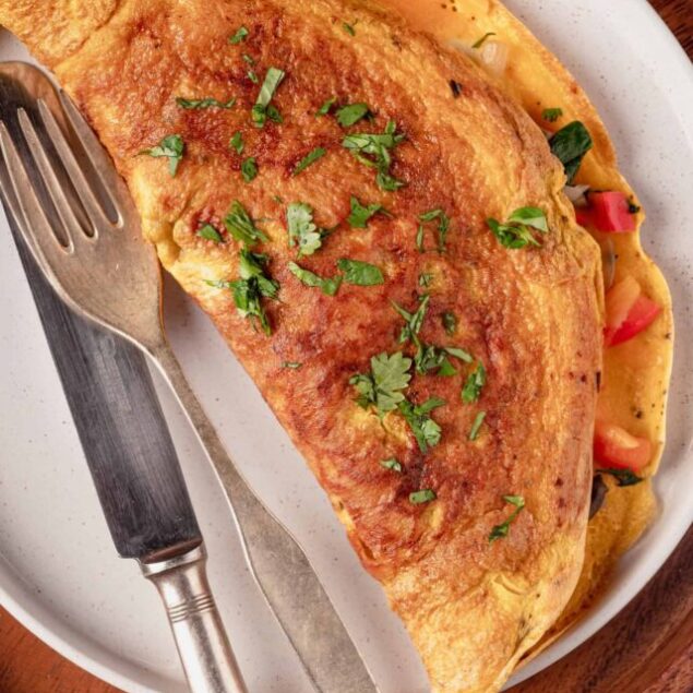 Golden-brown omelette with fresh herbs on white plate.