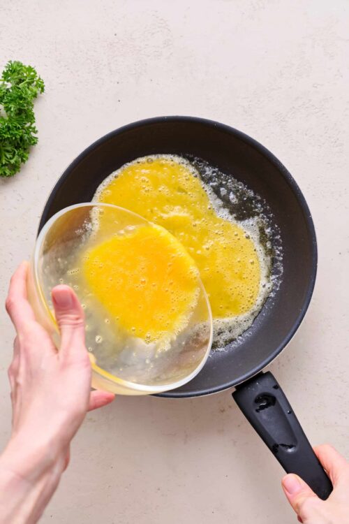 Fluffy scrambled eggs being poured into a skillet for breakfast recipe.
