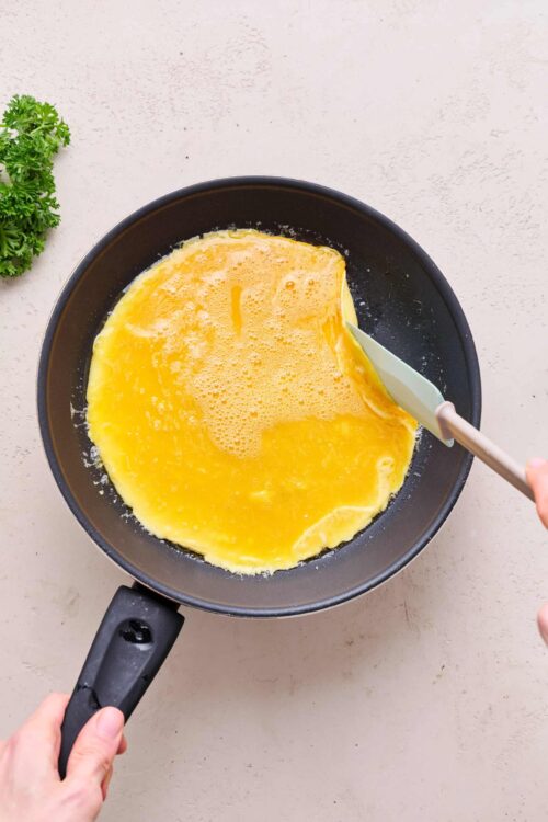 Fluffy scrambled eggs cooking in a black non-stick skillet.