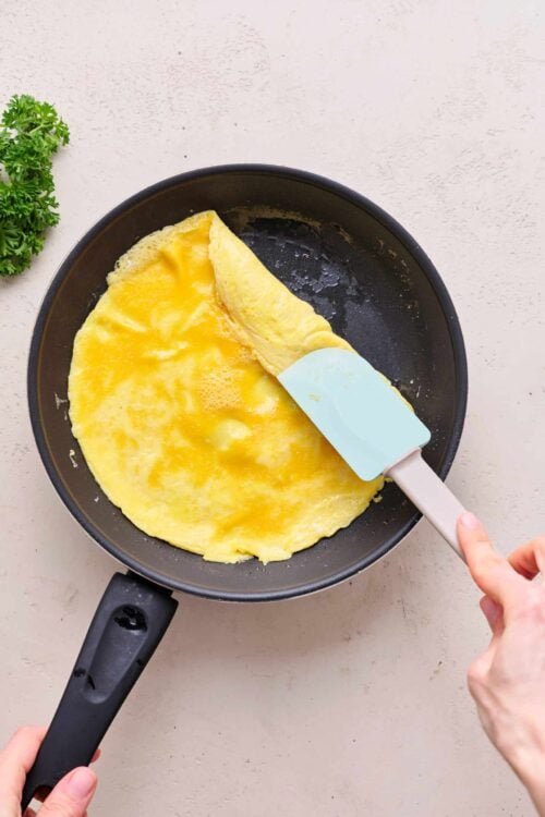Fluffy yellow omelette cooking in a black skillet with a spatula.