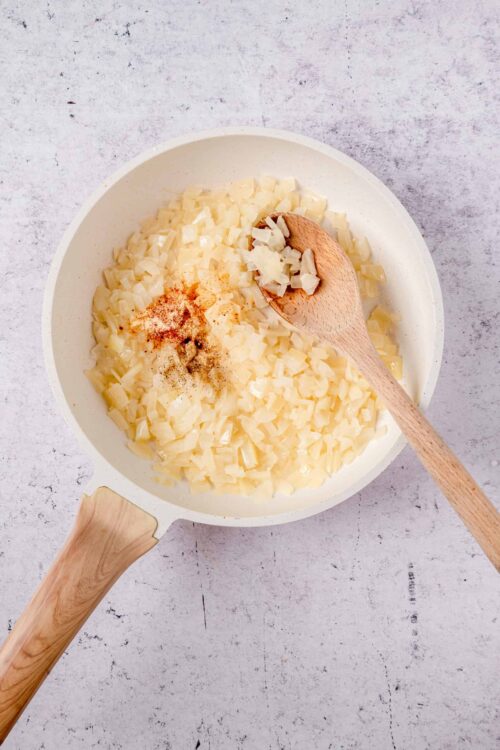 Diced onions in a white skillet with spices, ready for cooking.