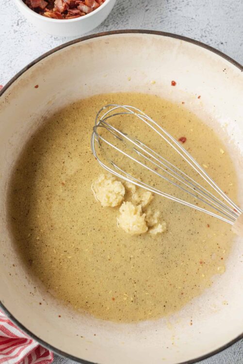 Butter melting in a saucepan with a whisk, cheese sauce preparation process.