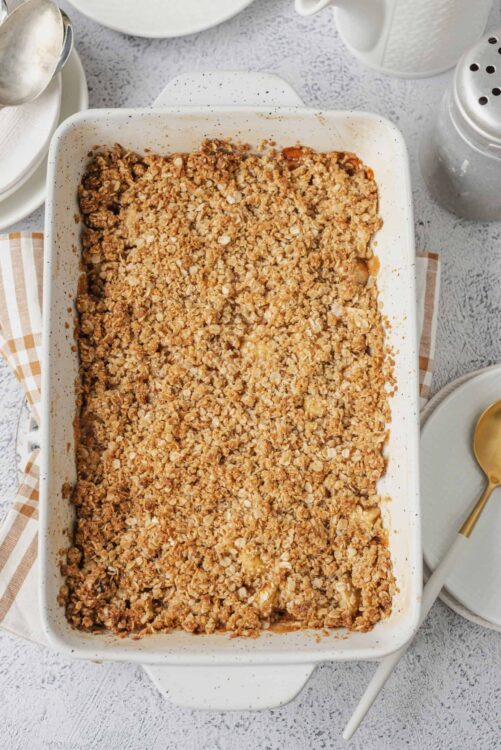 Crispy apple crumble baked dessert in a white casserole dish with golden oat topping.