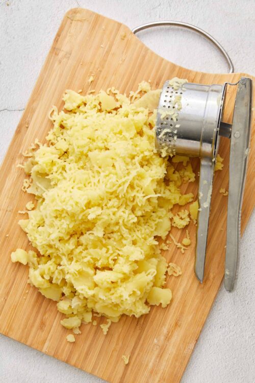 Fluffy mashed potatoes on a wooden cutting board with a potato masher, perfect for homemade baked potato recipes.