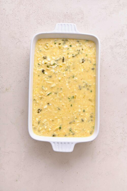 Creamy egg casserole with cheese and herbs in a white baking dish, ready to bake.