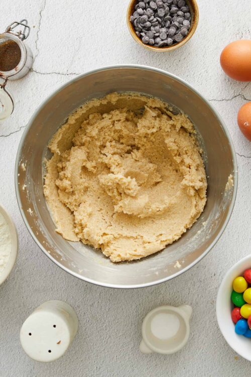 Creamy cookie dough in a mixing bowl, surrounded by baking ingredients and colorful candies.