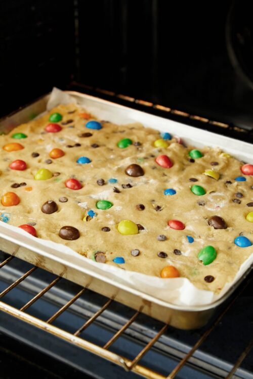 Colorful cookie dough with M&Ms and chocolate chips baking in oven.