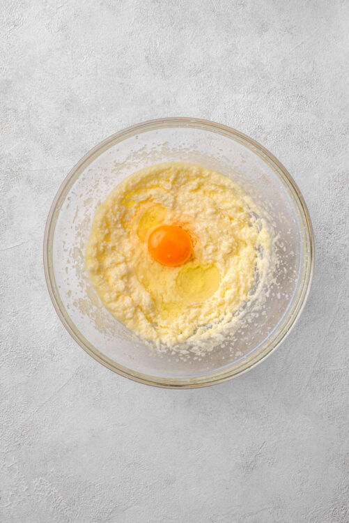 Cream cheese pound cake batter with egg in clear mixing bowl, ready to bake.