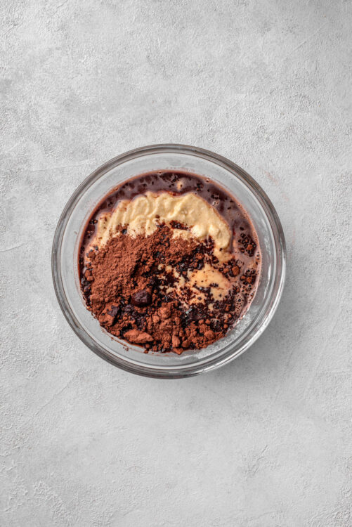 Cream cheese, cocoa powder, and chocolate mixture in a glass bowl for baking and dessert recipes.
