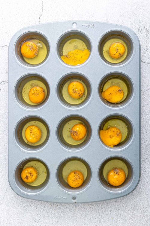 Vegan egg replacement in muffin tin with cracked eggs and black pepper seasoning.