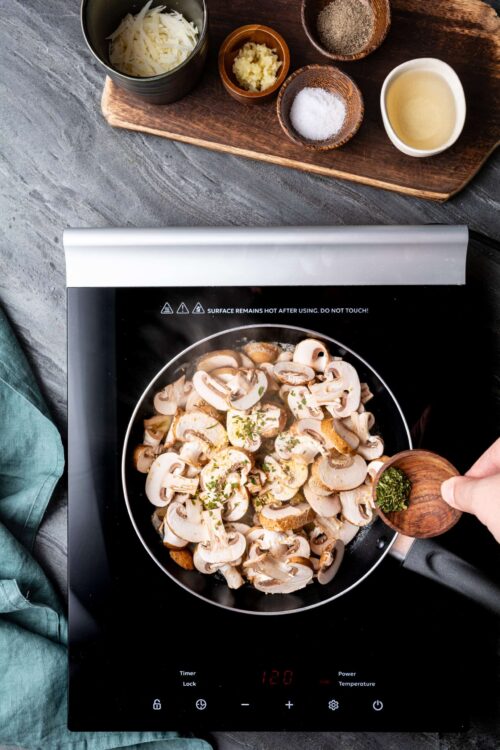 Sliced mushrooms cooking on induction stove with garlic and herbs.