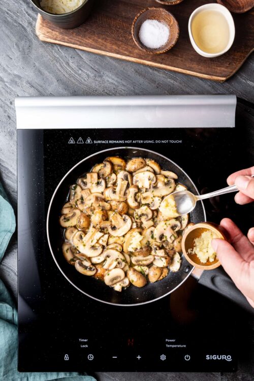 Sauteed mushrooms cooking on an induction stove, adding garlic for flavor.