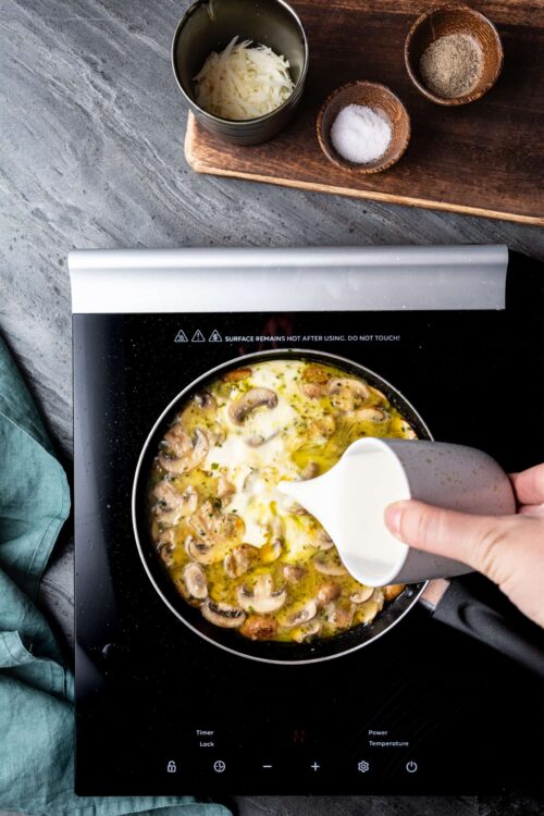 Creamy mushroom and egg scramble cooking on an induction cooktop, with shredded cheese and seasonings nearby.