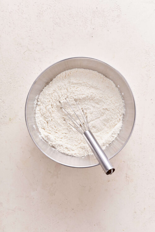 Flour in a stainless steel mixing bowl with whisk for baking bread or desserts.