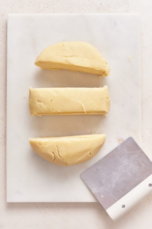 Soft, crumbly cheddar cheese on a white cutting board with a cheese slicer. Perfect for cheese and charcuterie boards or cooking.