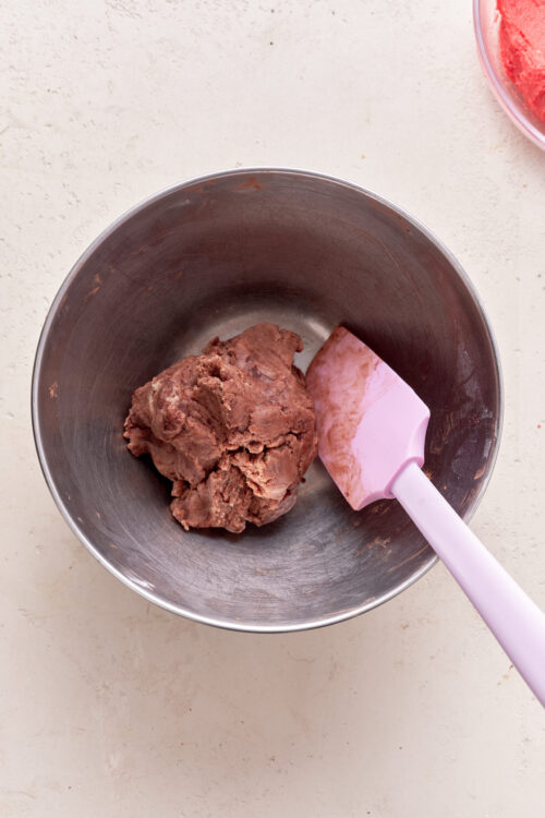 Softened cookie dough in a mixing bowl with pink spatula, ready for baking or shaping.
