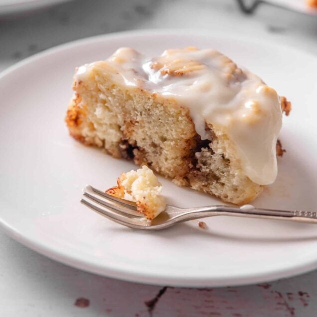 Moist cinnamon roll cake with cream cheese frosting on white plate.