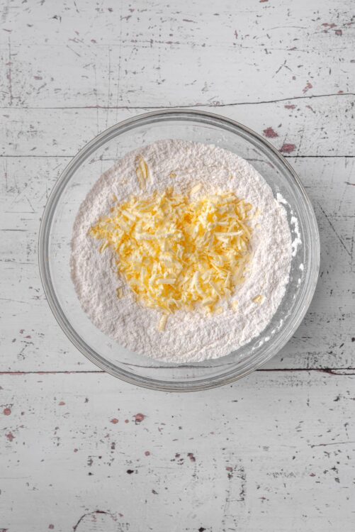 Flour and shredded cheese in a glass mixing bowl for baking or cooking.