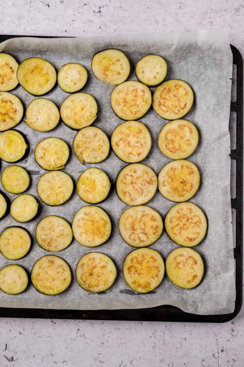 Sliced roasted eggplant on parchment paper prepared for baking.