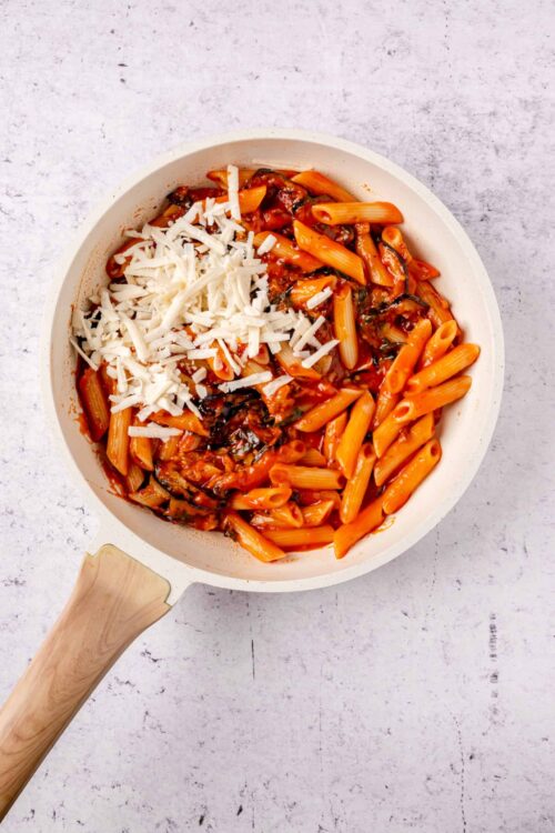 Creamy tomato pasta with shredded cheese in a white skillet.