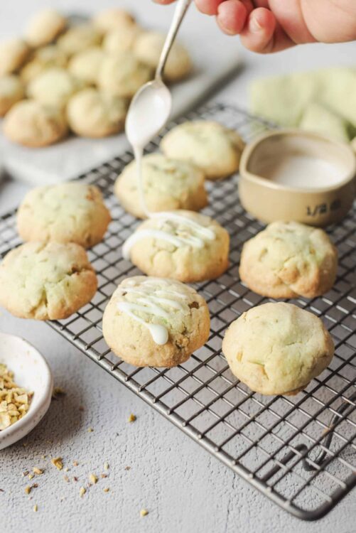 Buttery lemon cookies topped with white chocolate drizzle on a cooling rack.
