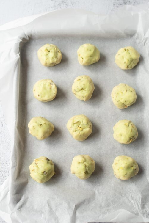 Soft pistachio and white chocolate cookie dough balls on parchment paper.
