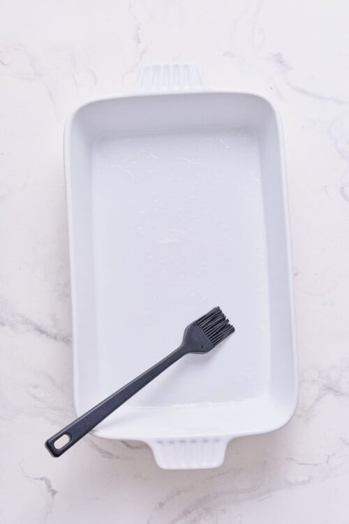 Ungreased white baking dish with a silicone basting brush inside for baking or roasting.