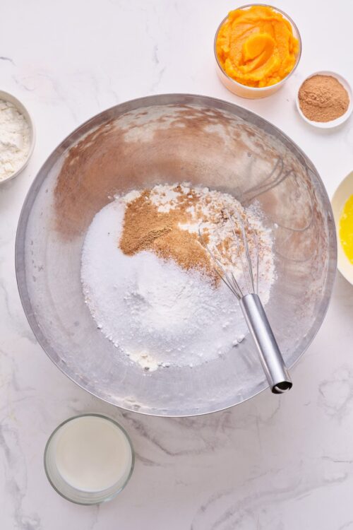Flour, sugar, spices, and dry ingredients in a mixing bowl for baking recipe.