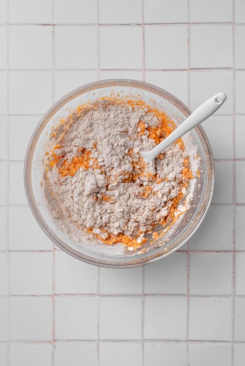 Flour and sweet potato mixture in glass bowl with white spatula, baking preparation.