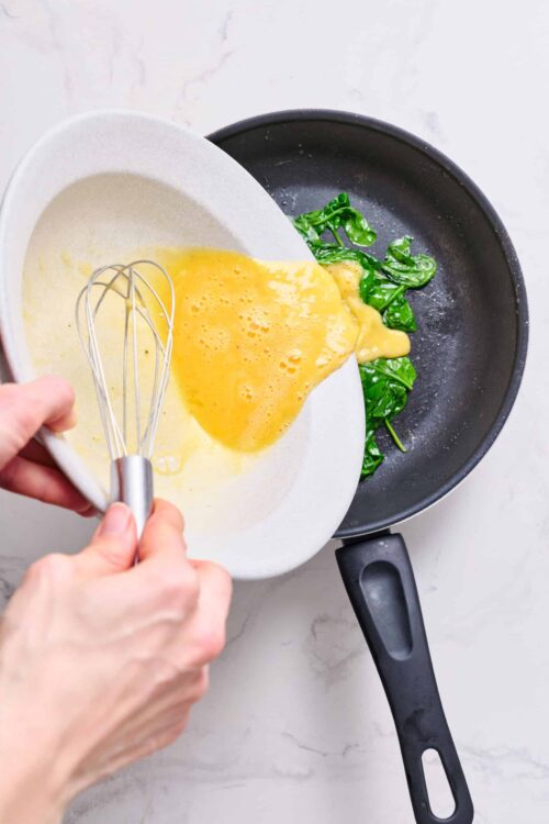 Creamy scrambled eggs with spinach cooking in a skillet.